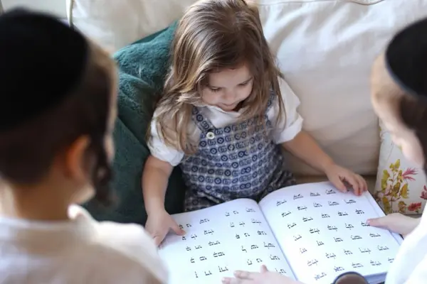 Little girl reading an alphabet book with her brothers, studio photography by Photoholic, Monsey NY