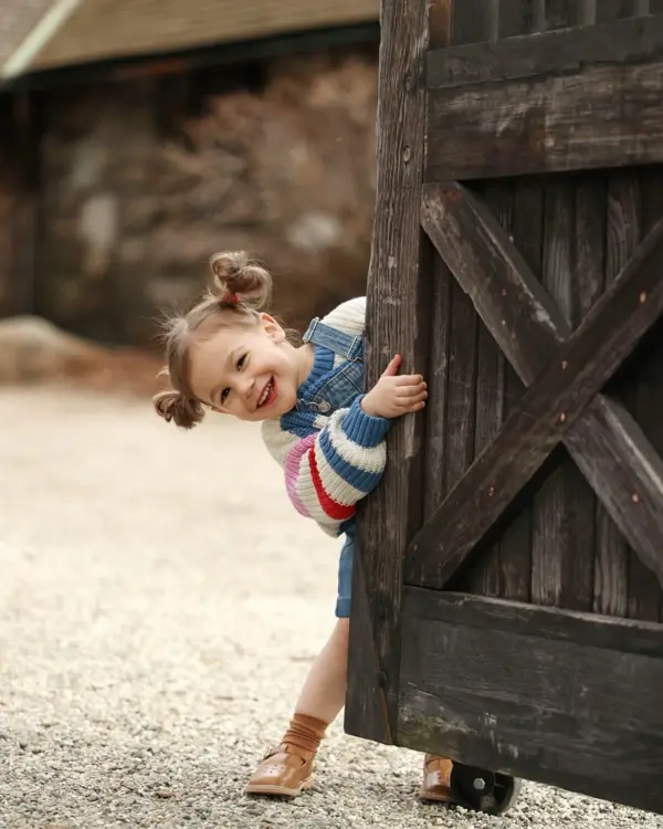 Laughing toddler peeking out from a wooden barn door, outdoor photography by Photoholic, Rockland County NY