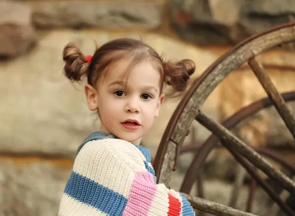 Toddler with pigtails by an old wagon wheel, outdoor photography by Photoholic, Rockland County NY