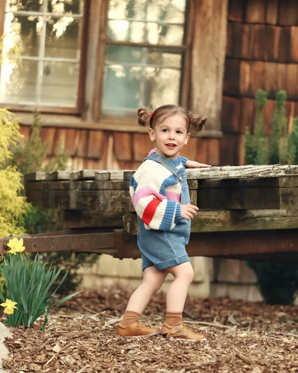 Toddler in a striped sweater outside a wooden cabin, outdoor photography by Photoholic, Rockland County NY